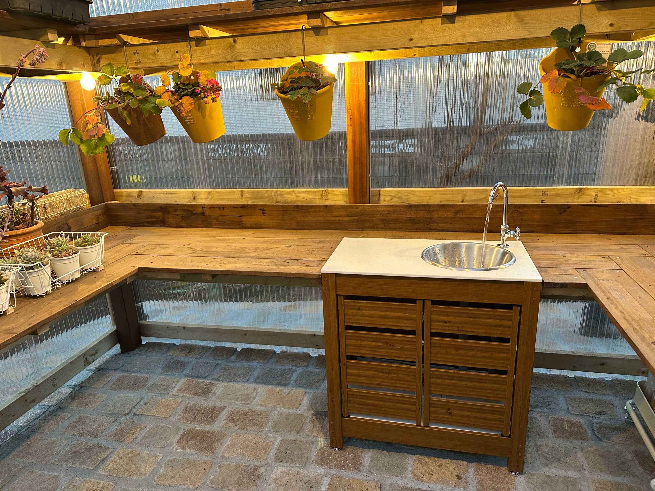 施工後の外構。シンクと木製の作業台を備えた、ハンギングポットの吊り下がるガーデニング用の屋根付きスペース