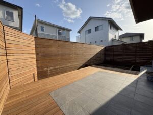 施工後の外構。木製フェンスに囲まれたウッドデッキとタイルデッキを組み合わせた住宅の裏庭