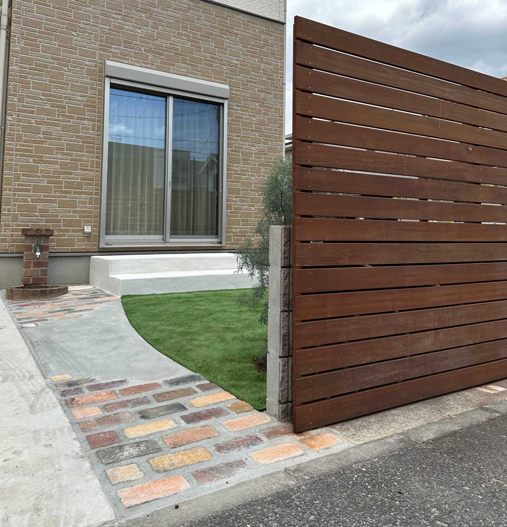 施工後の外構。木製フェンスとレンガの小道、人工芝の庭がある住宅
