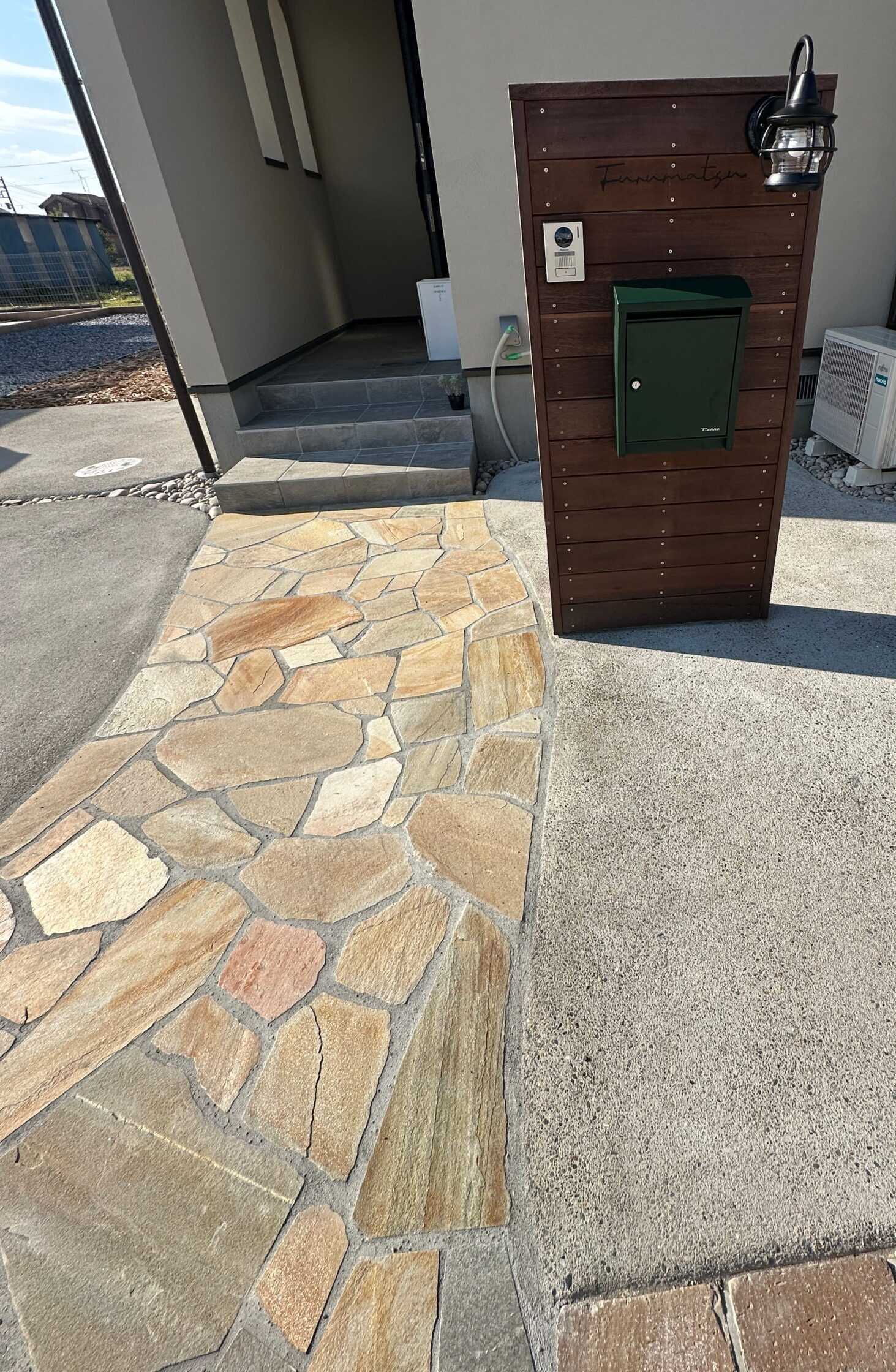 施工後の外構。乱形石調の小道と木製門柱のあるアプローチ