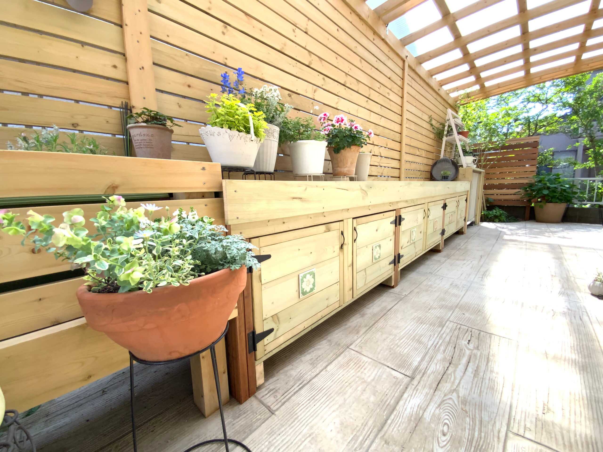施工後の外構。木製の作業台と鉢植えの花々が並ぶ、パーゴラ付きのテラス